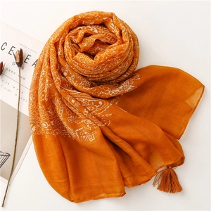 Detail of orange paisley print scarf with delicate fringe edges on a white background