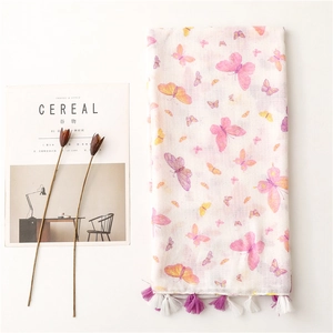 White linen-feel scarf with colorful butterfly prints and tassels next to dried flowers