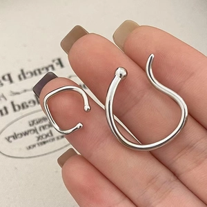 Macro shot of minimalist silver double-loop ear cuff held by hand over a card