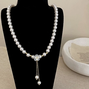 Détail du collier de perles blanches avec pendentif fleur et pompons dorés