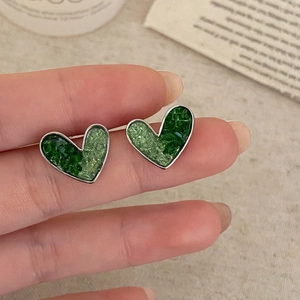 Elegant green crystal heart studs with silver metal frame held in hand for detail