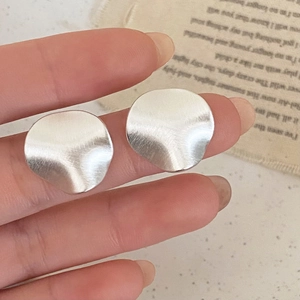 Detail of silver irregular wavy stud earrings with a brushed metal texture held by hand