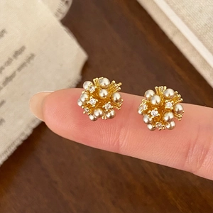 Detailed close-up of spherical gold stud earrings with pearls and zircon in hand