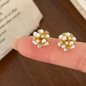 Detailed shot of starburst pearl and zircon stud earrings on gold base showing scale