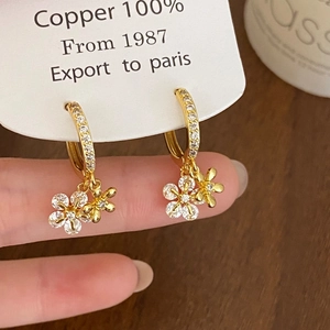 Détail de boucles d'oreilles fleur dorée avec zircons et artisanat en 100% cuivre