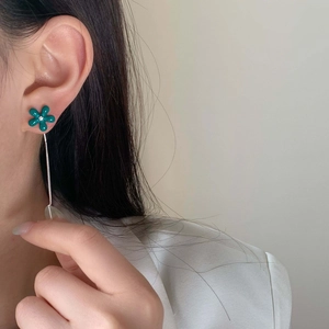Detail of blue-green flower drop earrings with long silver tassels on female model