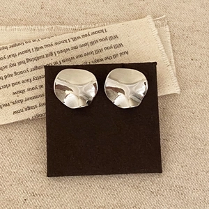 Détail de boucles d'oreilles argentées irrégulières avec finition métallique texturée