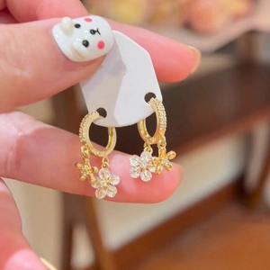 Détail des boucles d'oreilles fleurs dorées avec zircons portées pour montrer la taille