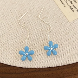 Detail of light blue flower drop earrings with silver tassels on beige linen fabric