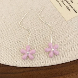 Detail of pink floral tassel earrings with long silver chains on a rustic wood surface