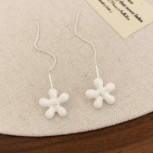 Macro detail of elegant white enamel five-petal flower drop earrings with silver chains