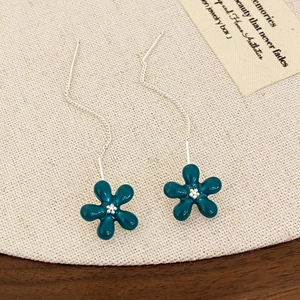 Detail view of long tassel earrings with dark green enamel petals on linen background