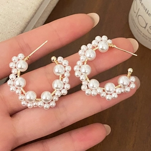 Elegant C-shaped earrings with white pearls and gold wire wrap on a warm wooden background