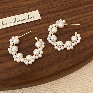 Handmade C-shaped pearl earrings with gold wire wrap on a vintage wooden tray