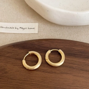 Minimalist gold hoop earrings with a matte brushed finish displayed on a dark wooden tray