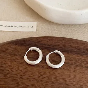 Minimalist matte silver hoop earrings with a brushed finish on a dark wooden stand