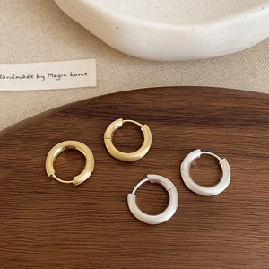 Detail view of gold and silver brushed metal hoop earrings on a walnut wood tray