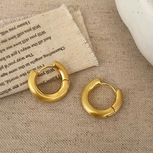 Detail of brushed gold hoop earrings with matte finish on beige linen background