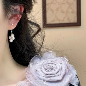Elegant pearl drop earrings worn with a large lilac fabric rose on the shoulder