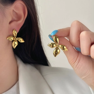 Close-up of golden petal stud earrings worn by model in elegant white blazer