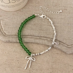 Detail of green beaded bracelet with silver bow pendant on beige fabric background