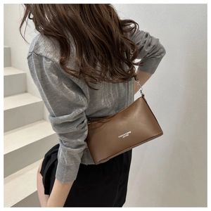 Brown leather bucket bag with white logo lettering shown worn as a stylish shoulder bag