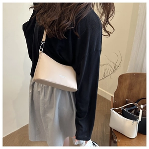 Sac à bandoulière minimaliste en cuir beige avec logo présenté dans un décor d'intérieur