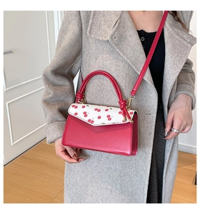 Red crossbody bag with cherry print flap worn over a stylish grey wool coat