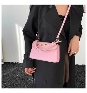 Pink shoulder bag featuring red strawberry prints and a knotted handle detail on model