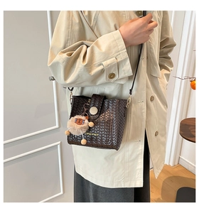 Detail der gewebten Beuteltasche in Dunkelbraun mit Modetext und Plüschbär-Anhänger