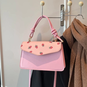 Chic pink trapezoid handbag featuring strawberry print flap and unique knotted handle