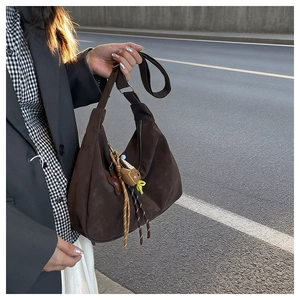 Detail of dark brown faux suede crescent shoulder bag with bear charm and adjustable strap