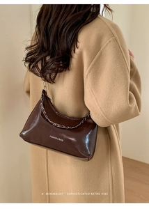 Detail of dark brown glossy hobo bag with silver chain and white text on wool coat