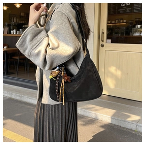Detail of black suede hobo bag with cute bear charm and tassel in a street scene