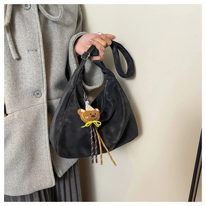 Detail view of a black half-moon tote bag with a cute bear charm and adjustable shoulder strap