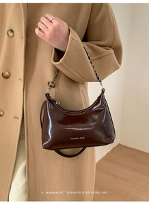Detail of dark brown glossy moon bag with metal chain strap and logo lettering
