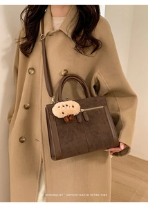 Detail of dark brown suede tote bag featuring gold zippers and a plush bear charm