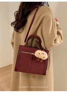 Detail view of burgundy faux suede tote bag with metal zipper and plush charm