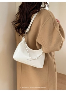 White PU leather tote bag with silver chain worn over a camel wool coat in detail