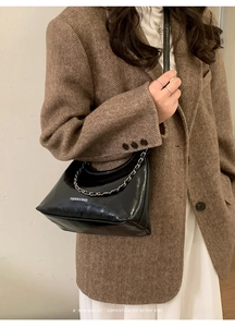 Detail of glossy black leather tote bag with silver chain and white fashion branding