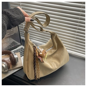 Detail of khaki hobo shoulder bag featuring a decorative dark brown braided tassel charm