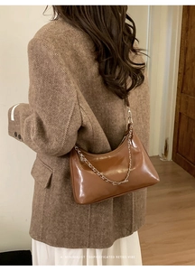 Detail of a brown crescent-shaped faux leather tote bag with silver chain and shoulder strap