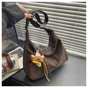 Detailed close-up of a brown suede tote bag with a cute bear charm and wide shoulder strap
