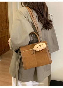 Close-up of brown suede tote bag featuring a gold zipper and plush cookie charm