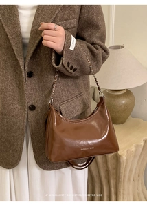 Detail of glossy brown chain tote bag with embossed text on textured wool blazer