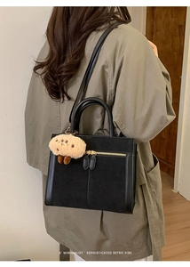 Detail of black suede tote bag with gold zippers and a plush charm on the handle