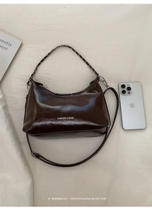 Detail of dark brown glossy leather tote bag with silver chain strap and fashion logo