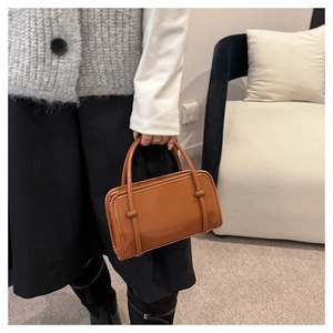 Detailed view of caramel leather handbag with FASHION embossing and knot handle details