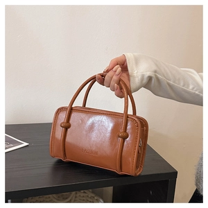 Close-up of caramel brown minimalist handbag featuring embossed fashion text and dual handles