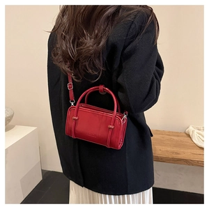Detailed view of a shiny red crossbody bag with embossed text on a black wool coat